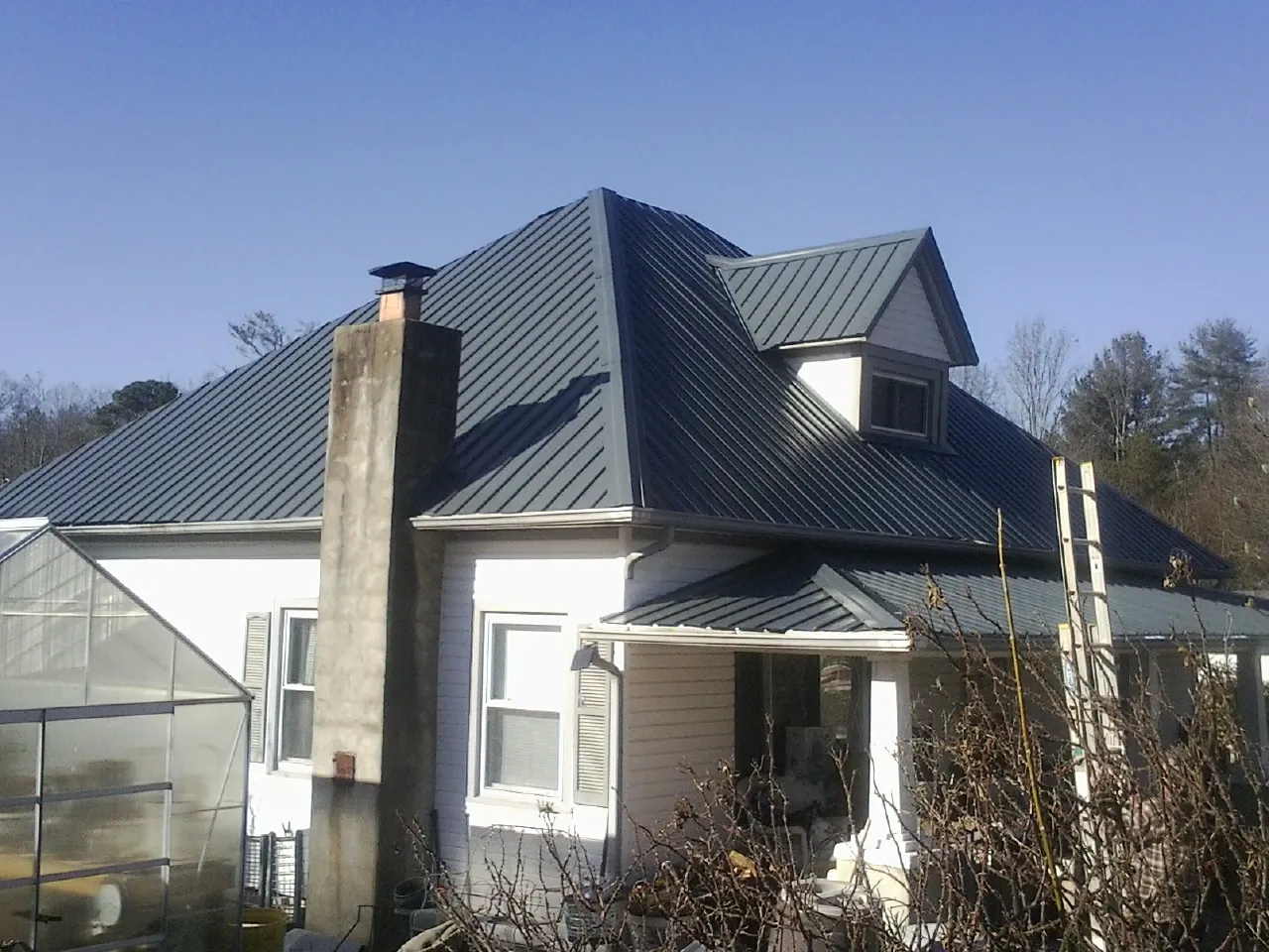 Dark blue standing seam metal roof on a white farmhouse with dormer — Slate & Tile Roof Repair by Roofing Brothers in Cable