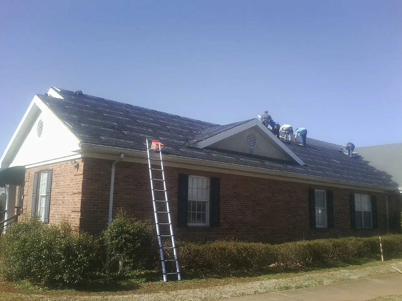 Crew tearing shingles off a brick ranch roof with a ladder set — Metal Roof Repair work by our crew in Cable