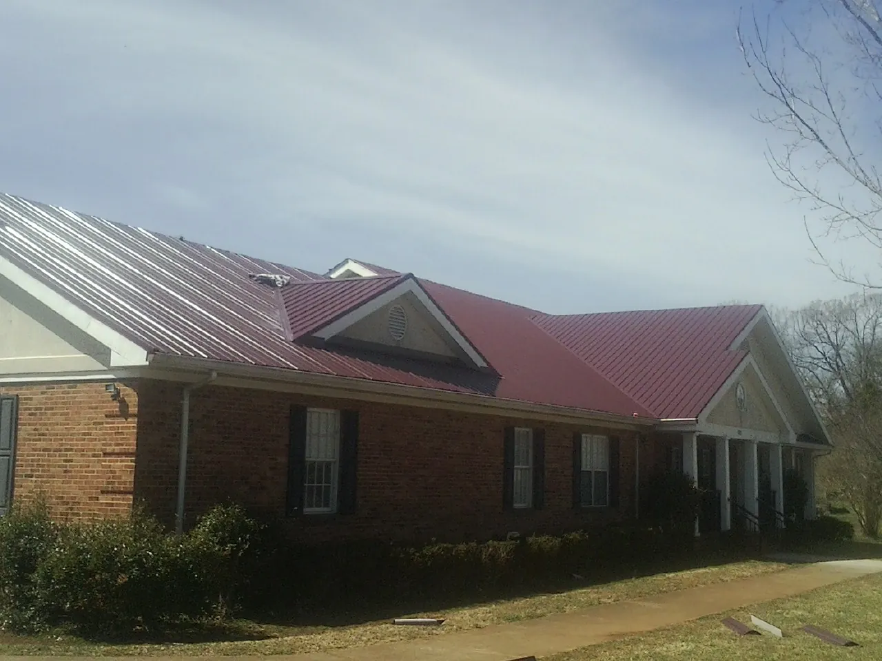 Red metal roof with gabled entries on a long brick building, from a Hail Damage Roof Repair job in Cable