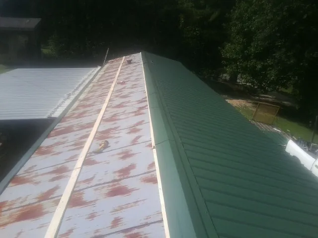 Old rusted panels beside newly installed green metal roofing — Wind Damage Roof Repair by Roofing Brothers in Cable