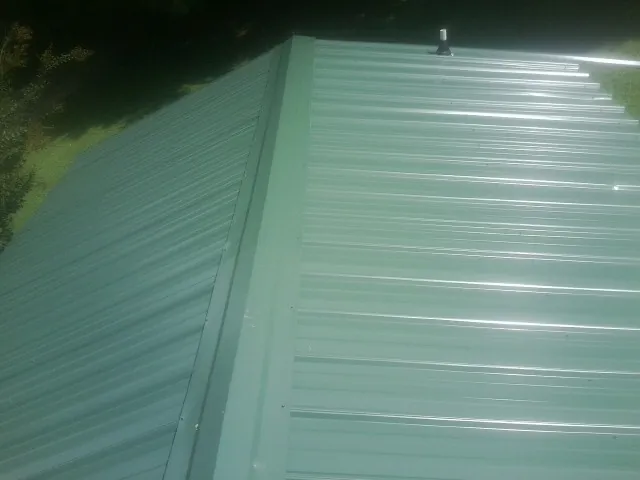 New green metal panels meeting at the ridge of a roof — Flat Roof Repair work by our crew in Cable