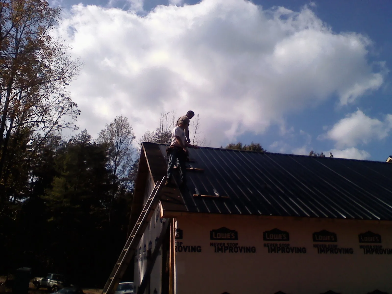 Roofer fastening dark metal panels high against a cloudy sky, from a Roof Inspection job in Cable