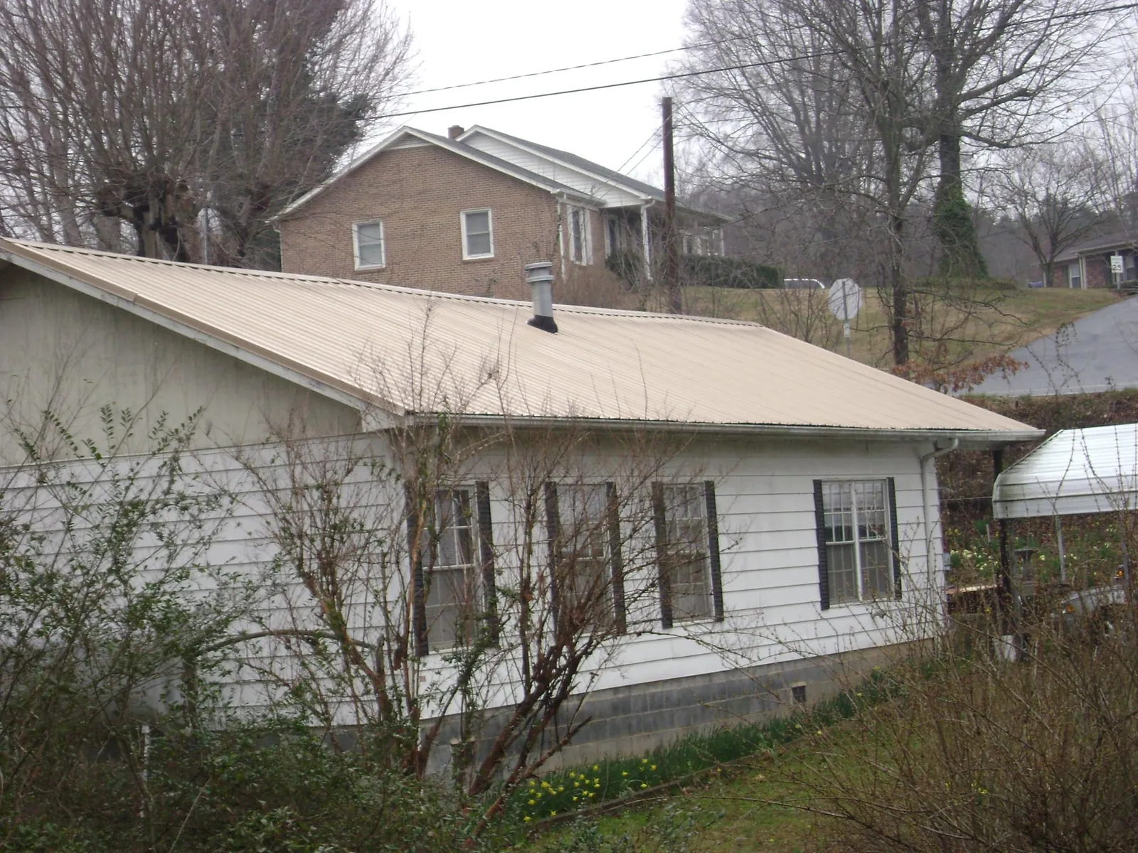 Tan metal roof on a white sided house set into a hillside — Commercial Roofing by Roofing Brothers in Cable