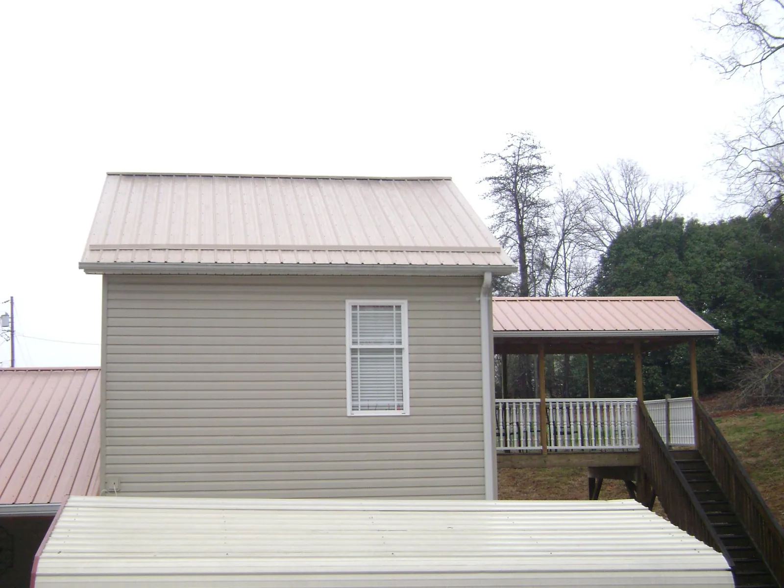 Tan metal roofs on a two story addition and attached porch, from a Roof Replacement job in Cable
